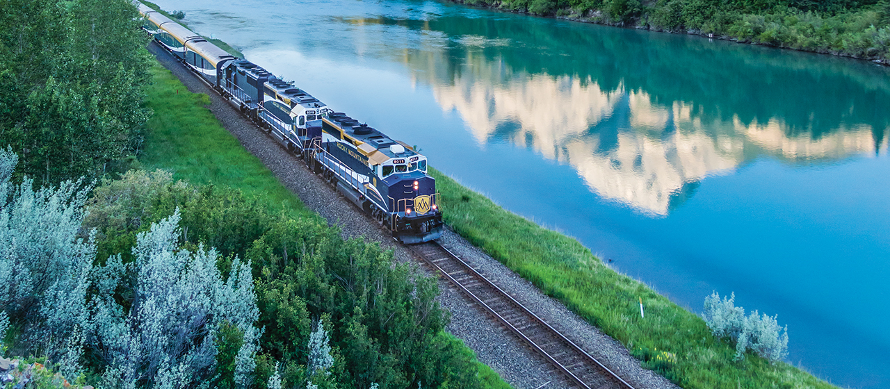 Luxury train travelling alongside a turquoise lake in the Canadian Rockies